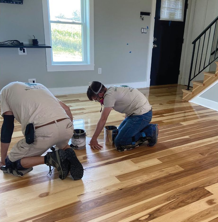 Two men are kneeling on a wooden floor staining a living room floor Galebach’s Floor Finishing