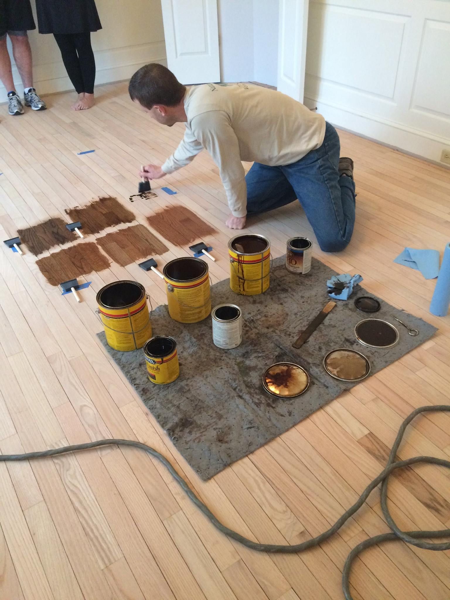 A man is kneeling on the floor with buckets of paint Galebach’s Floor Finishing