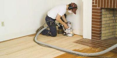 A man is sanding a wooden floor with a vacuum cleaner.