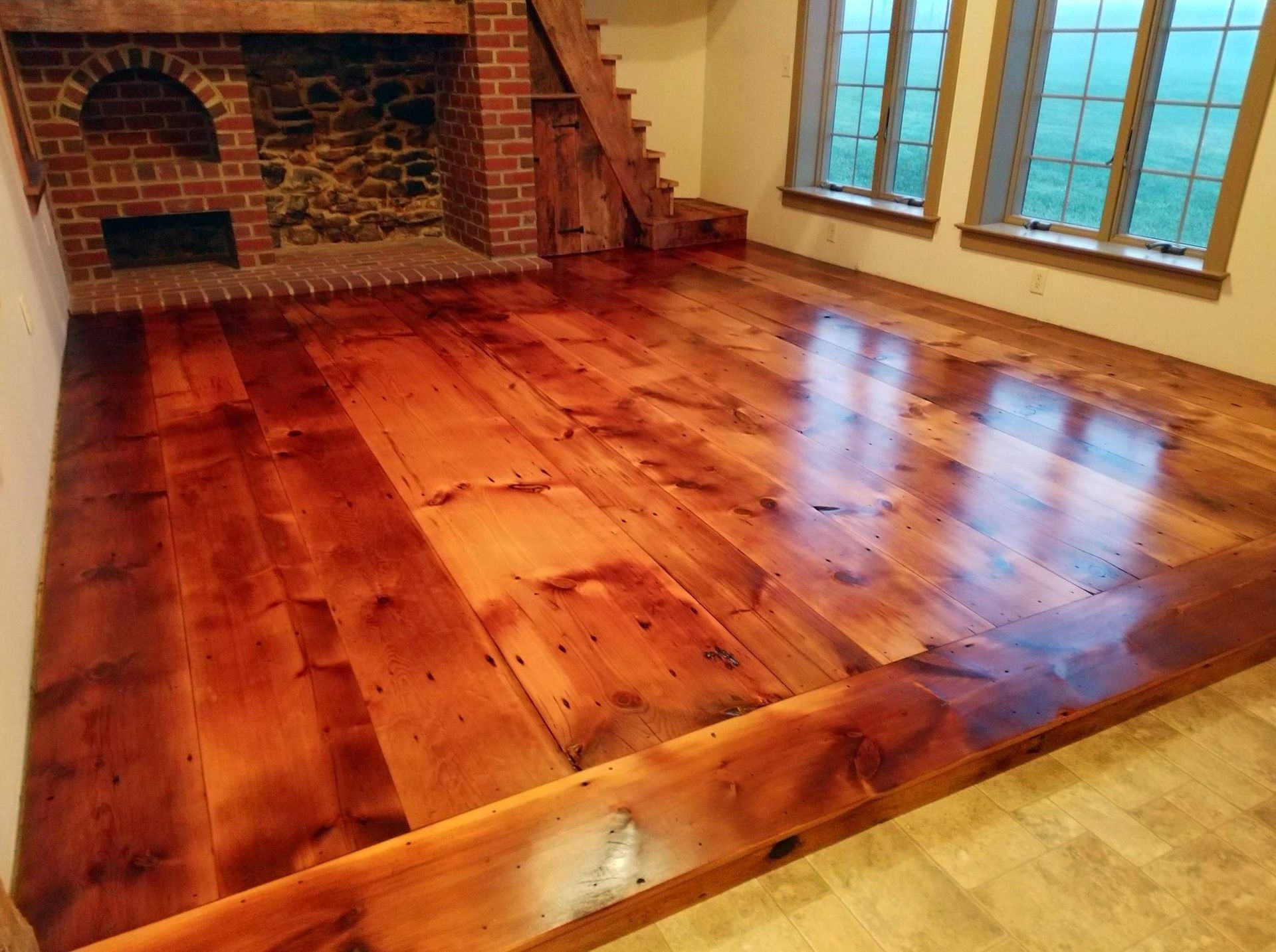 A living room with a refinished wooden floor and a brick fireplace Galebach’s Floor Finishing