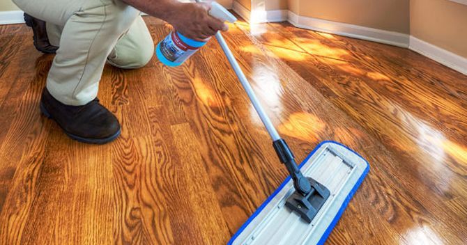 A man is cleaning a wooden floor with a mop.