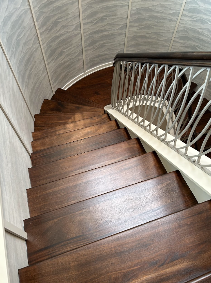 A spiral staircase with wooden steps and a metal railing by Galebach’s Floor Finishing