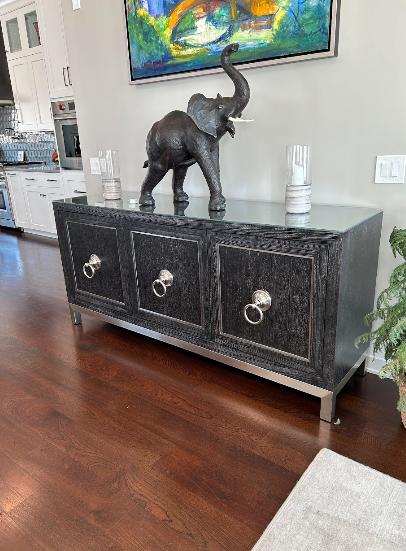 A statue of an elephant is sitting on top of a black dresser in a living room.