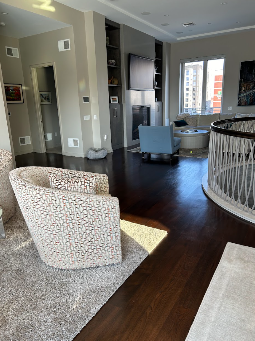 A living room with two chairs , a rug , a fireplace and a staircase Galebach’s Floor Finishing.