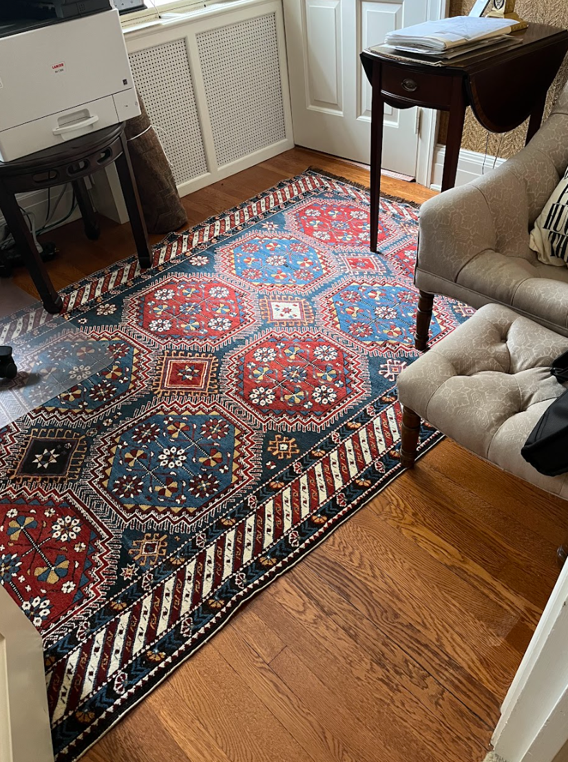 A living room with a rug , chair , table and ottoman.