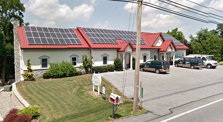 A white building with a red roof and solar panels on it.