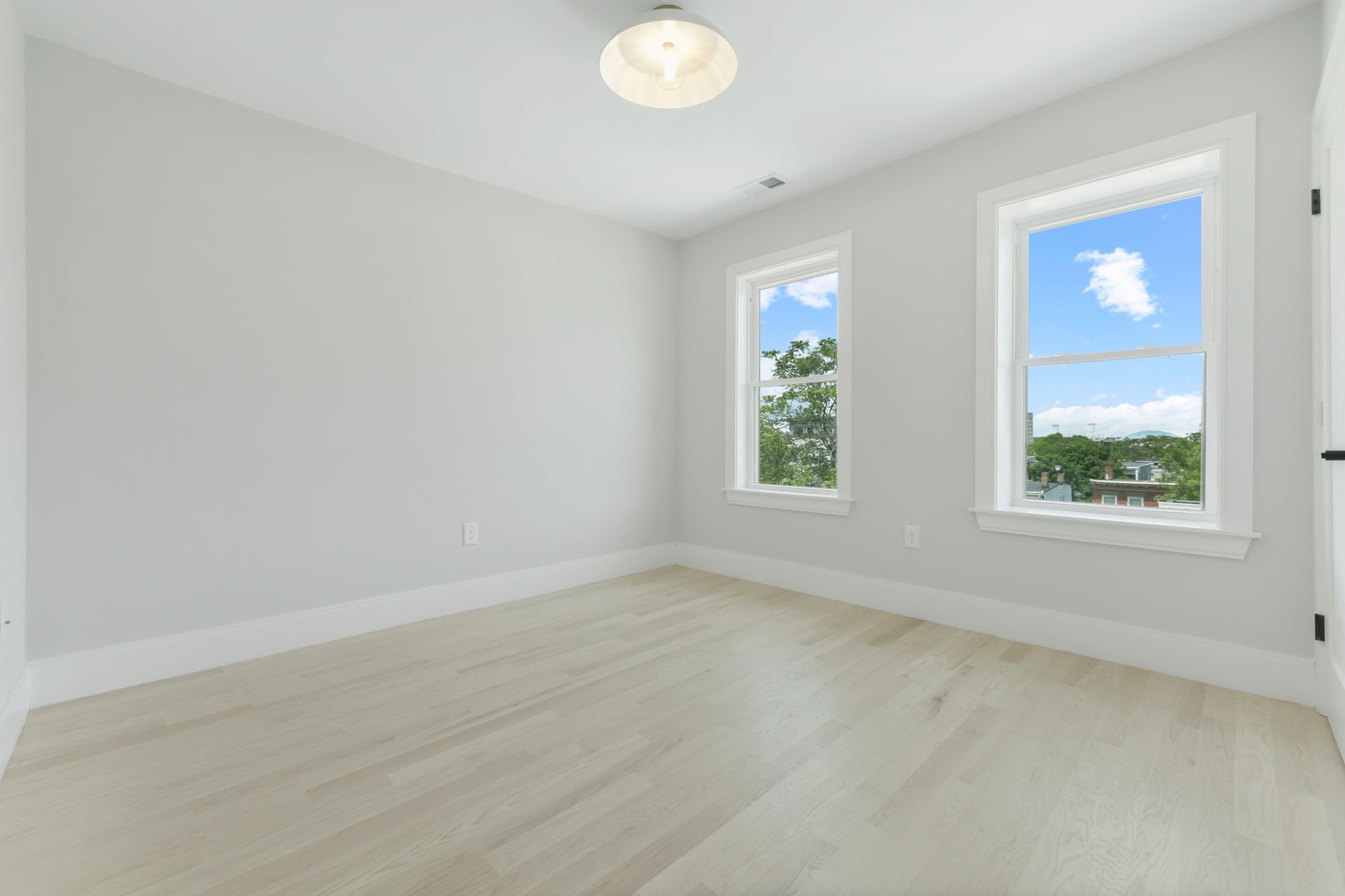 An empty room with two windows and hardwood floors.
