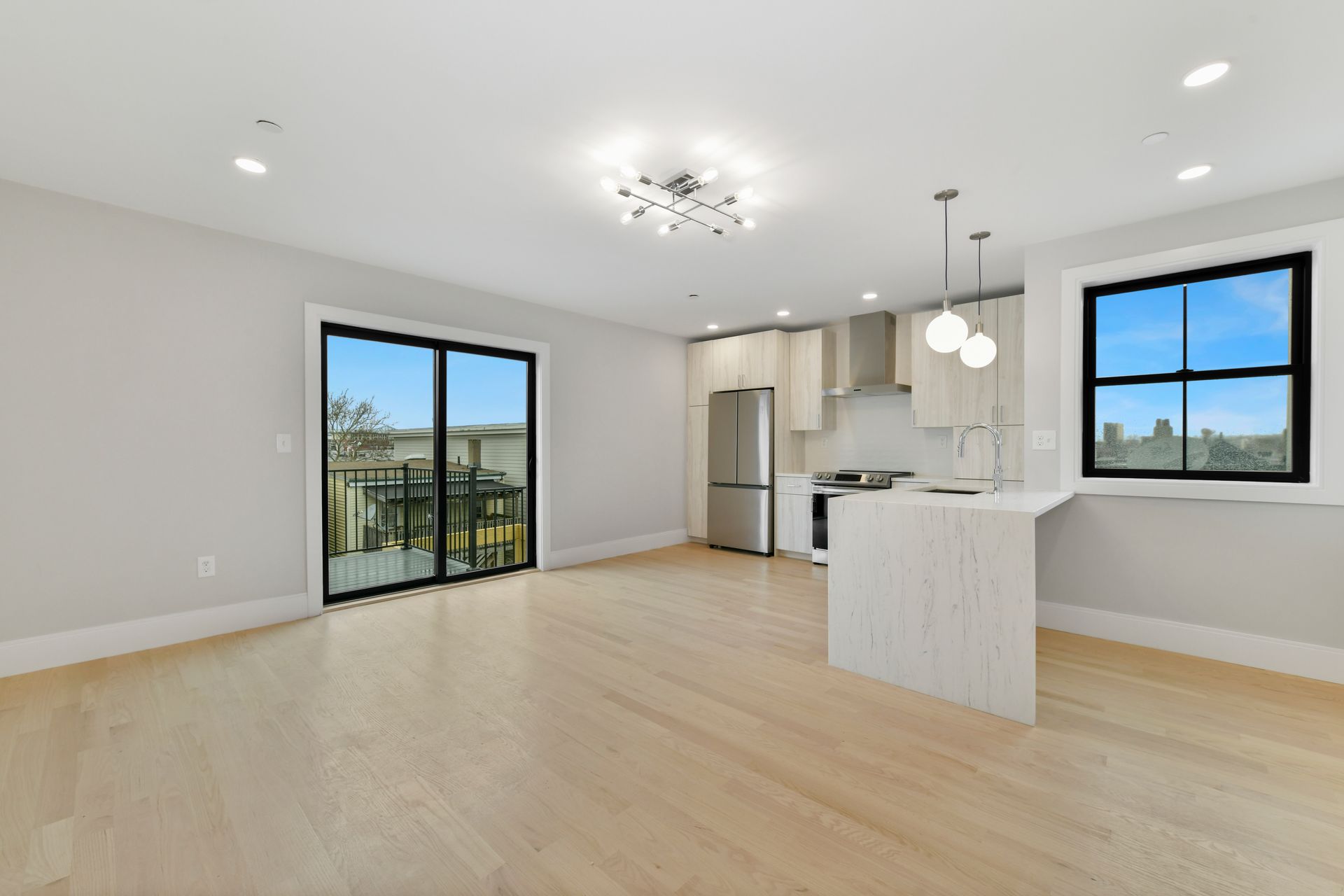 An empty living room with hardwood floors and sliding glass doors leading to a kitchen.