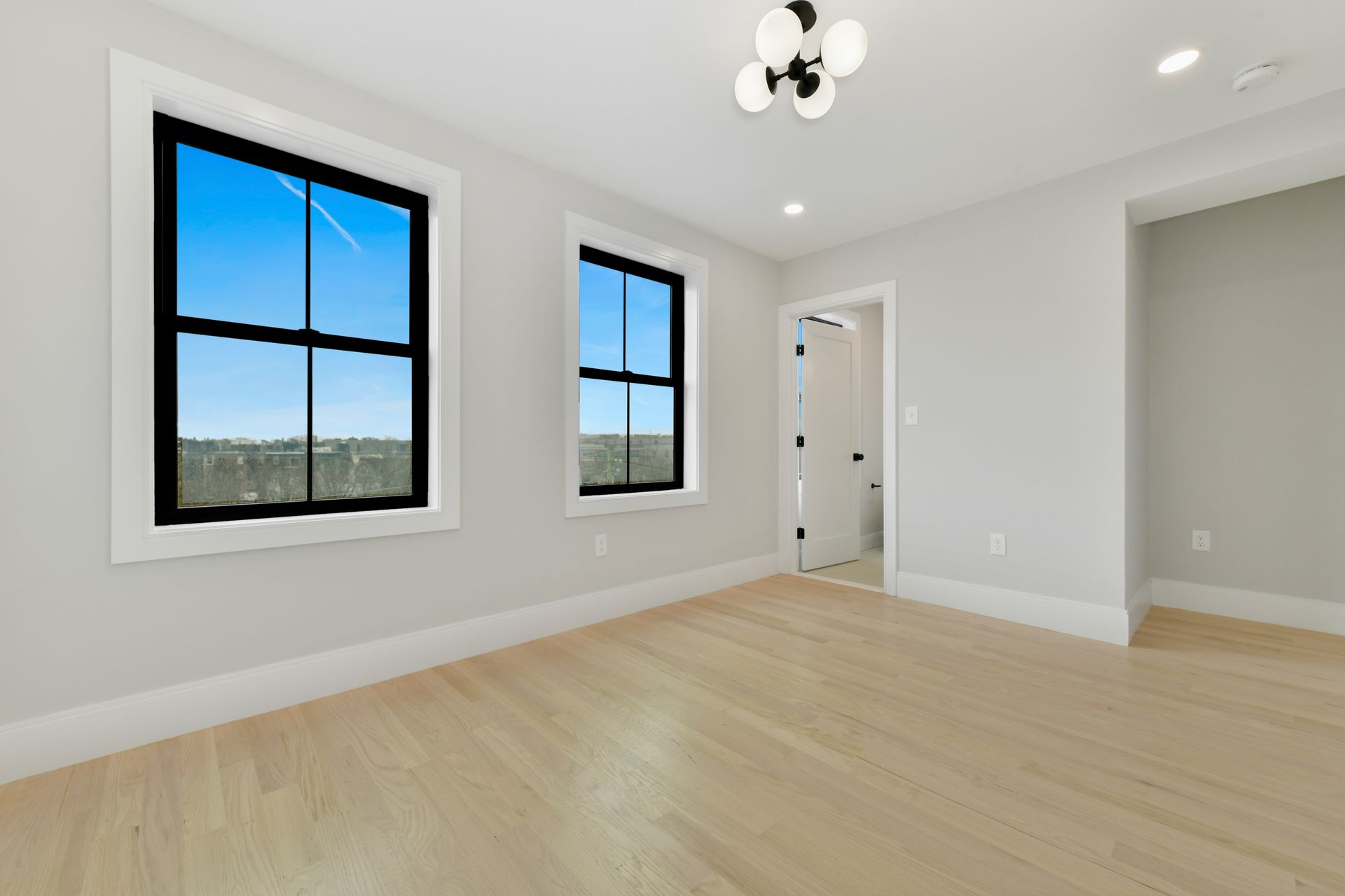 An empty room with two windows and hardwood floors.