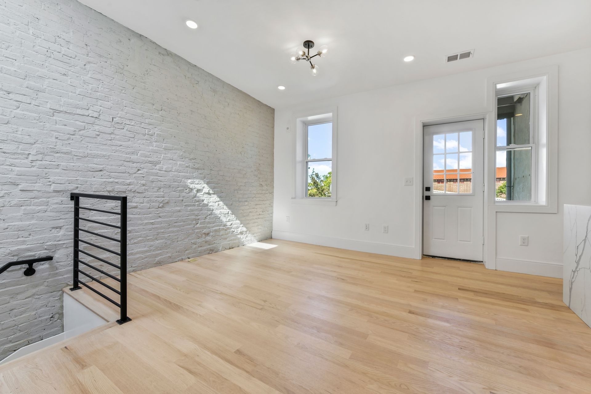 An empty living room with hardwood floors and a white brick wall.