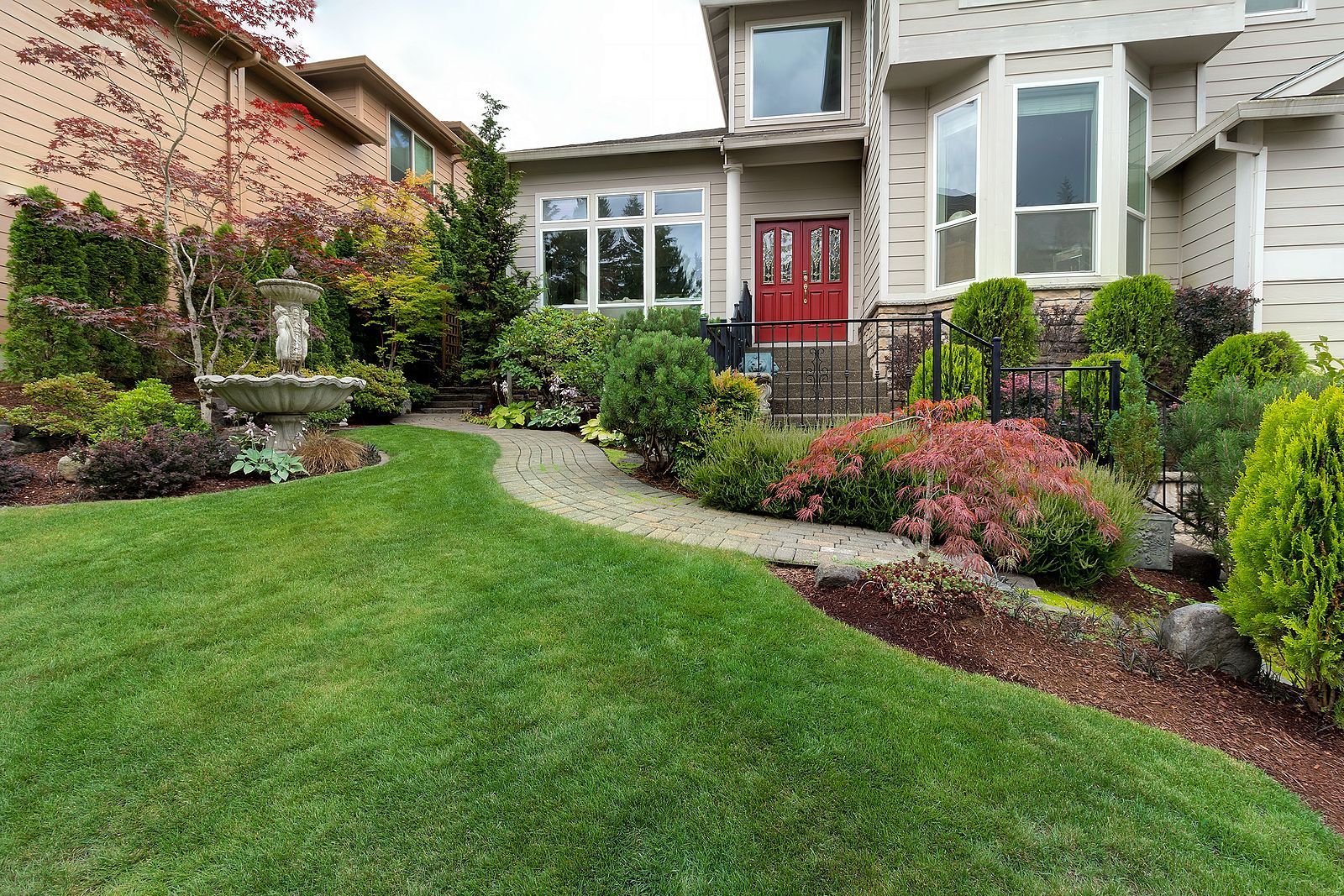 Curated front yard with stone path, red door, and fountain.