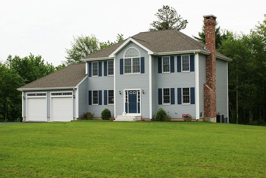 Two-story blue house with a lush green lawn and bushes.