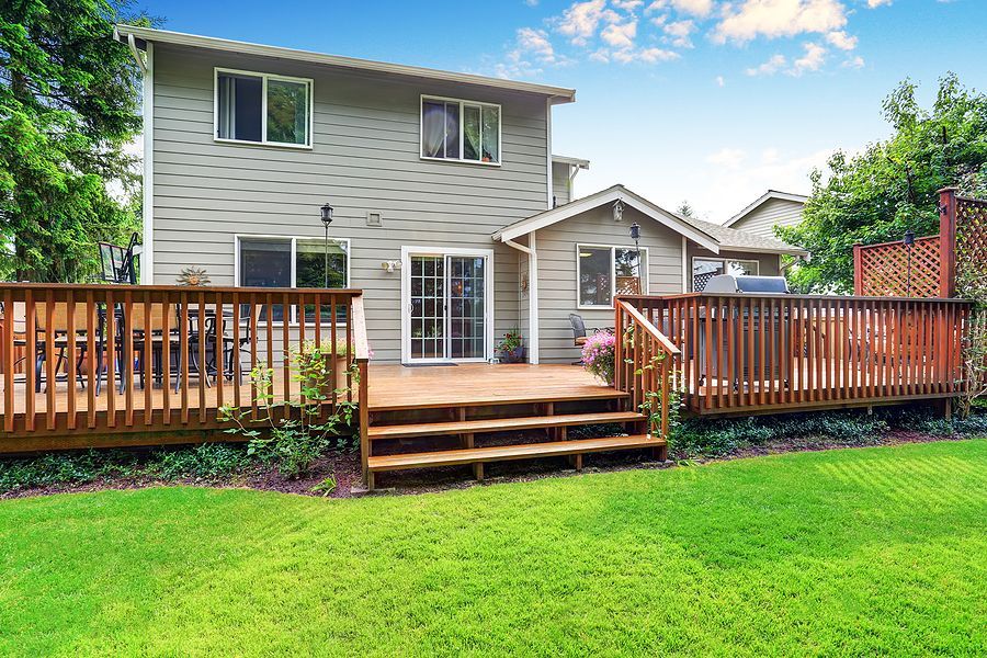 Two-story gray house featuring a large wooden deck and lawn.
