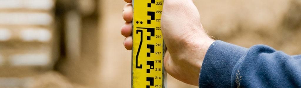 Una persona sostiene una vara de medir amarilla al aire libre. La vara tiene marcas negras.