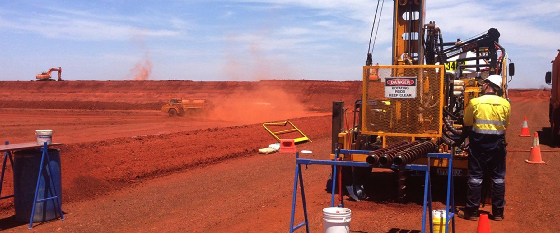 Sitio de construcción con maquinaria pesada, nubes de polvo naranja y un trabajador con equipo de protección.