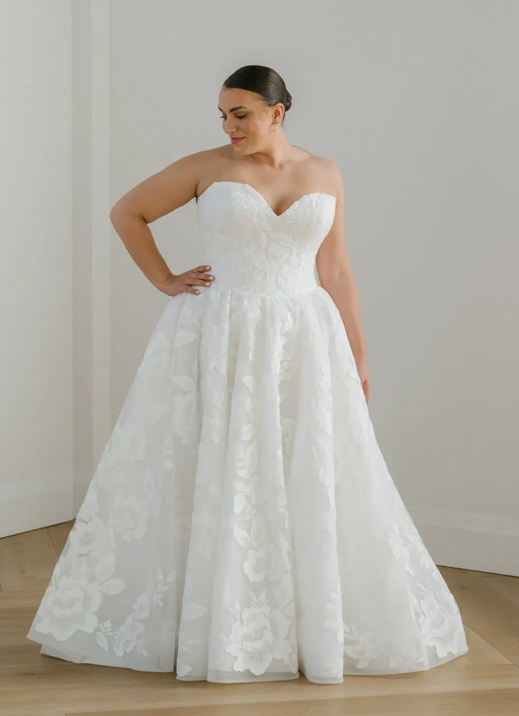 Bride in white wedding dress, holding up skirt, standing in a studio.