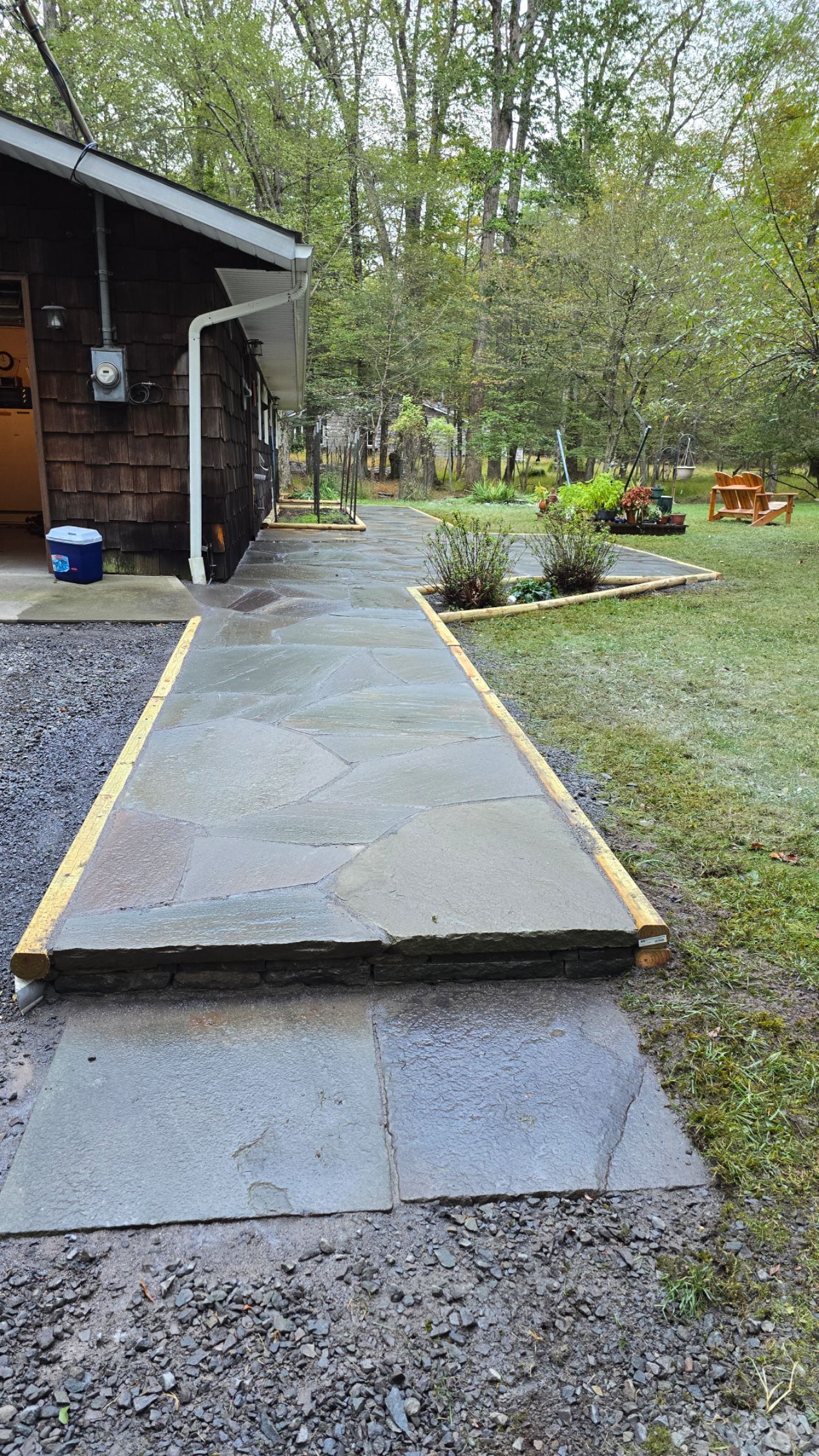 A concrete walkway leading to a house in the woods.