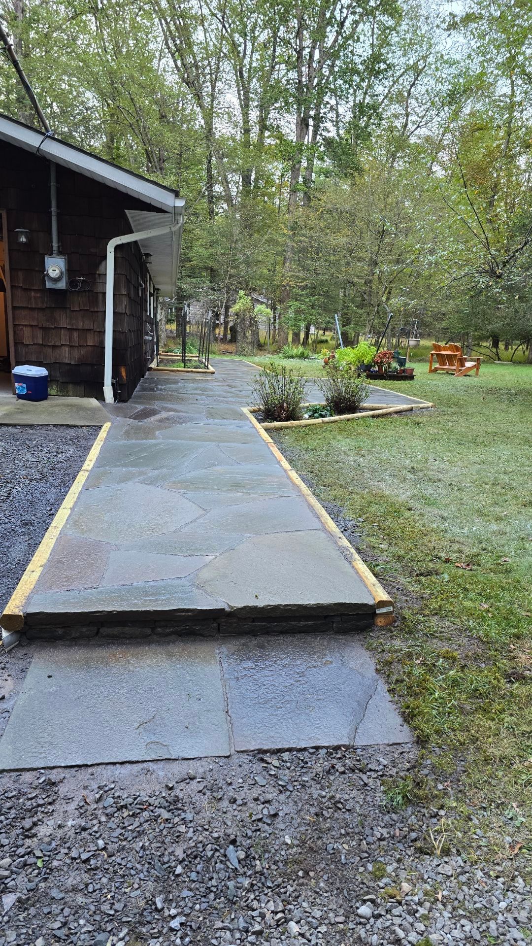 A concrete walkway leading to a house in the woods.