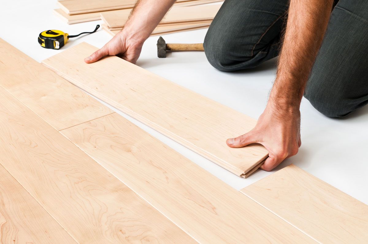 A man is kneeling down to install a wooden floor.