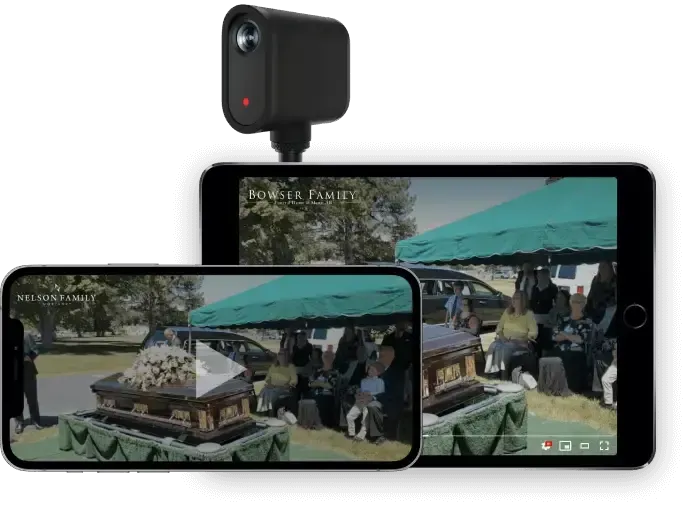 A small camera mounted above a tablet and phone displaying a live-streamed funeral service with people gathered outdoors.
