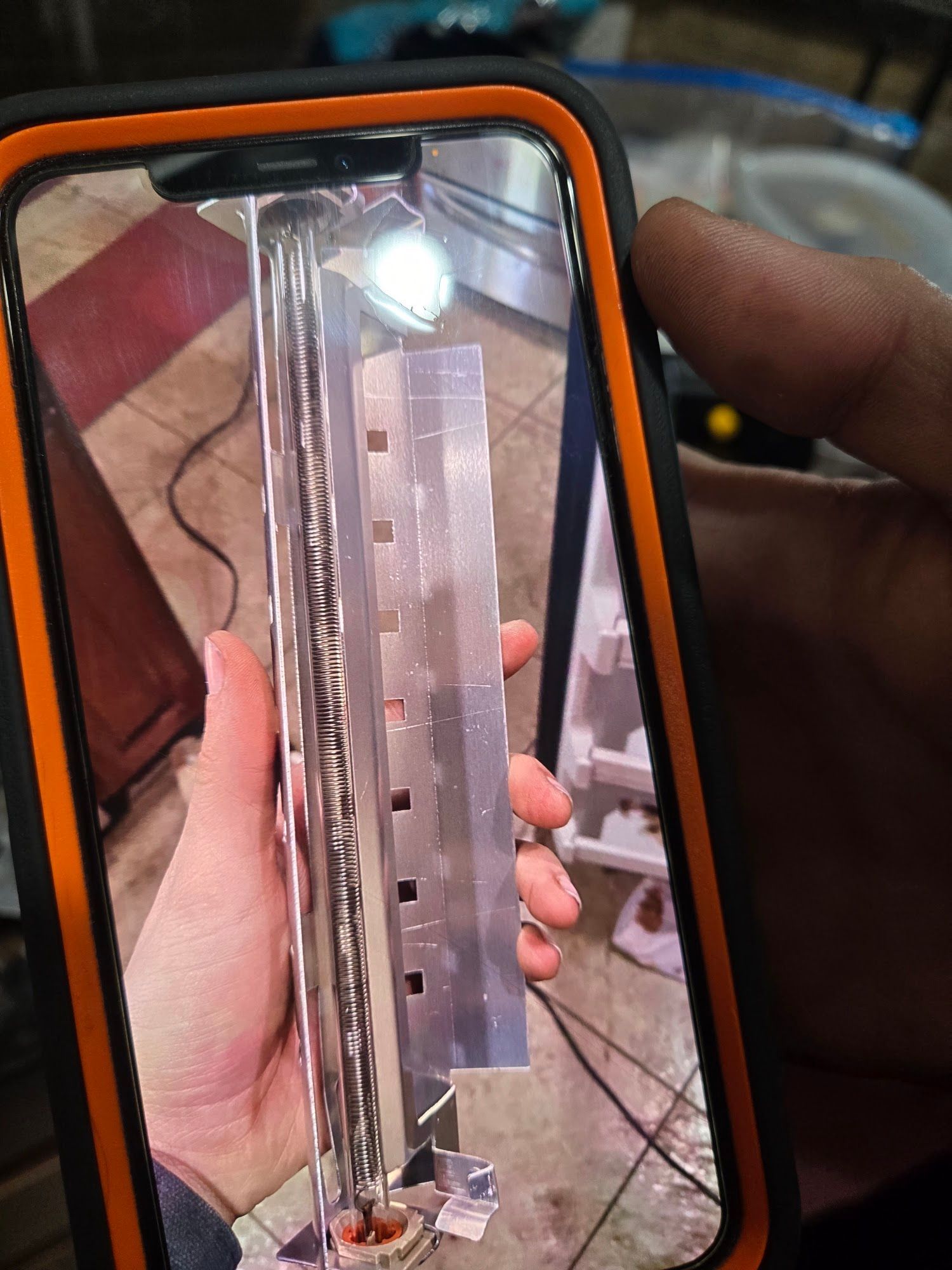 Person holding a metal part, photographed through a phone screen; part has rectangular notches.