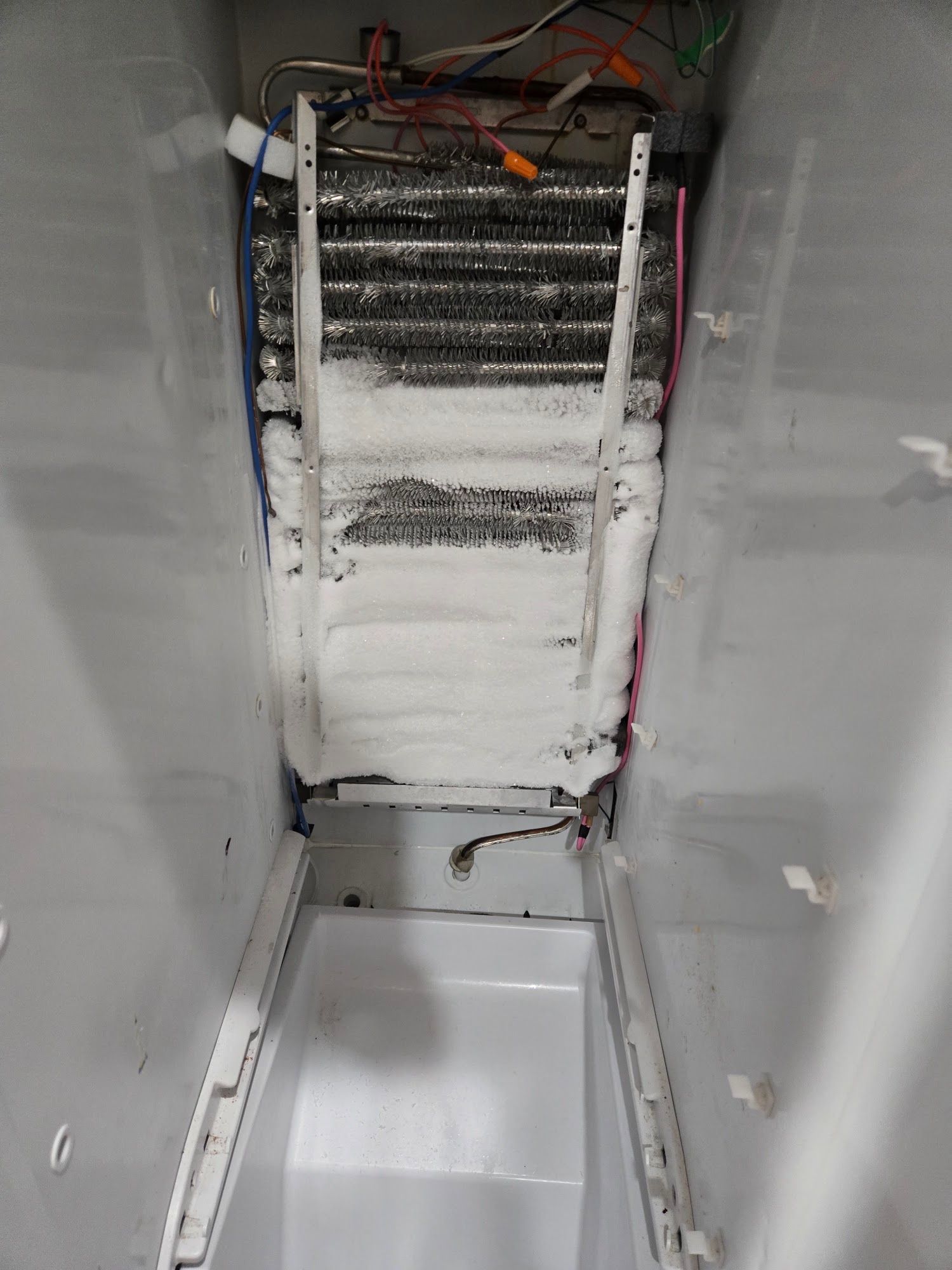 Refrigerator freezer interior covered in frost, showing coils and racks.