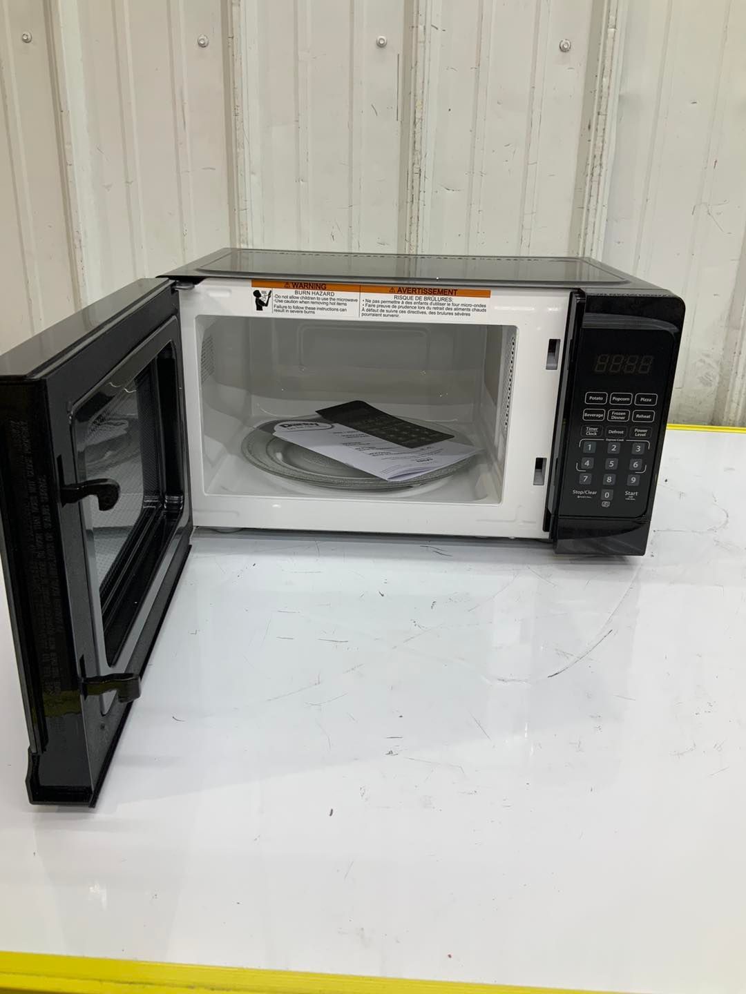 A black microwave oven with the door open is sitting on a white table.