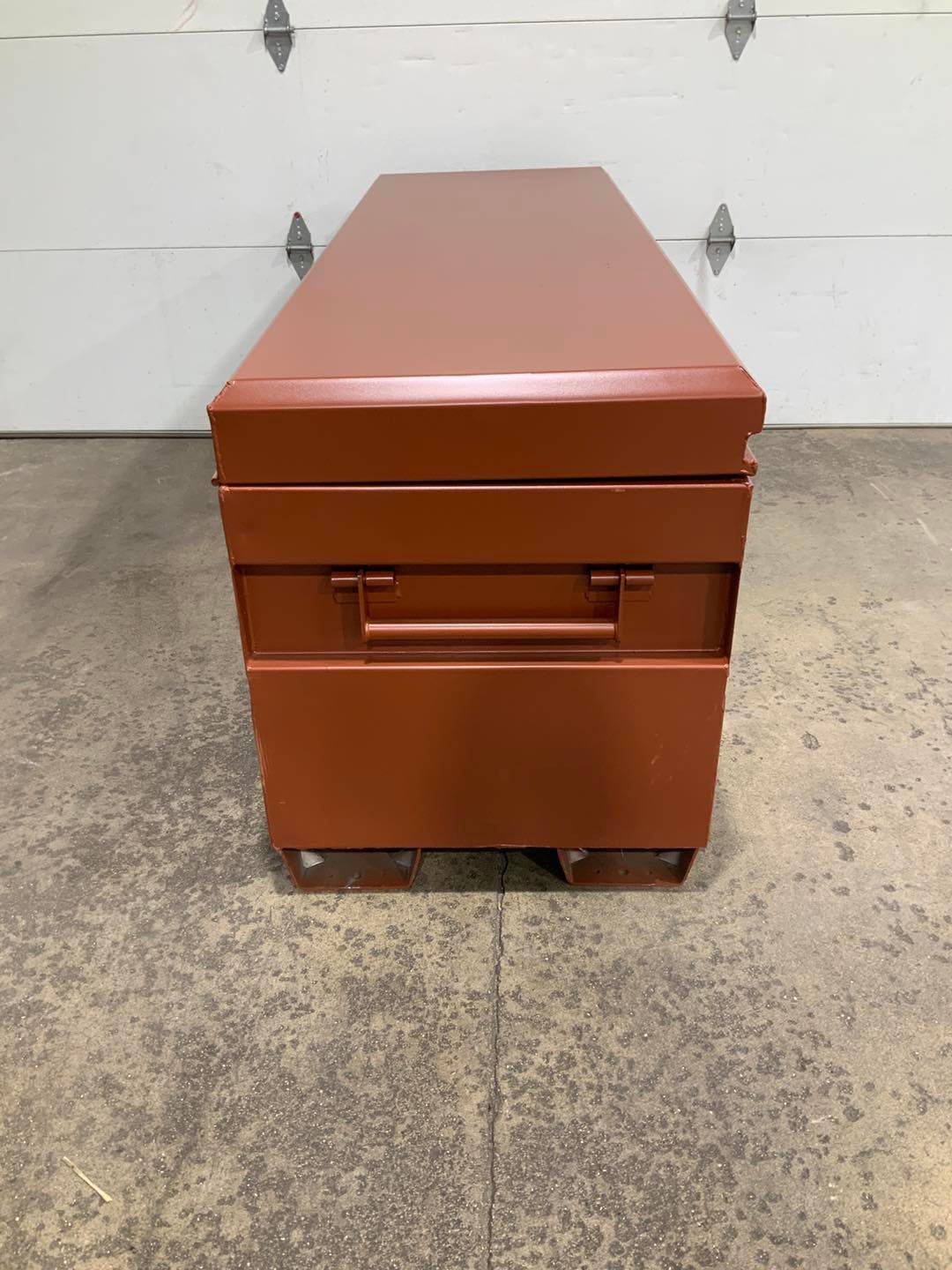 A red metal box is sitting in front of a garage door