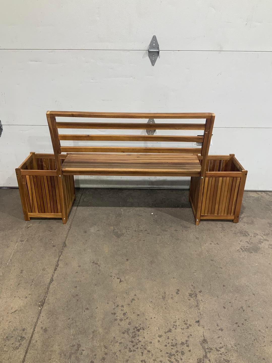 A wooden bench with two planters attached to it is sitting in front of a garage door.