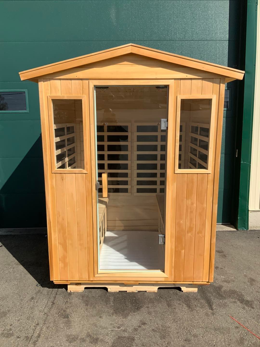 A wooden sauna is sitting in front of a green garage door.