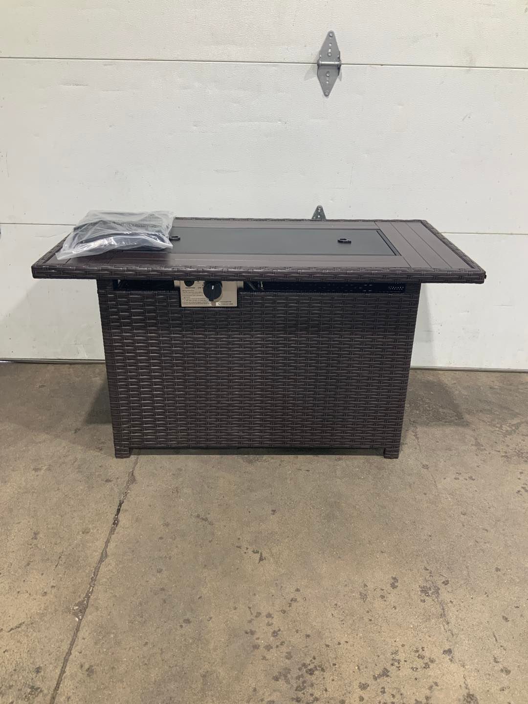 A wicker fire pit table is sitting in front of a garage door.