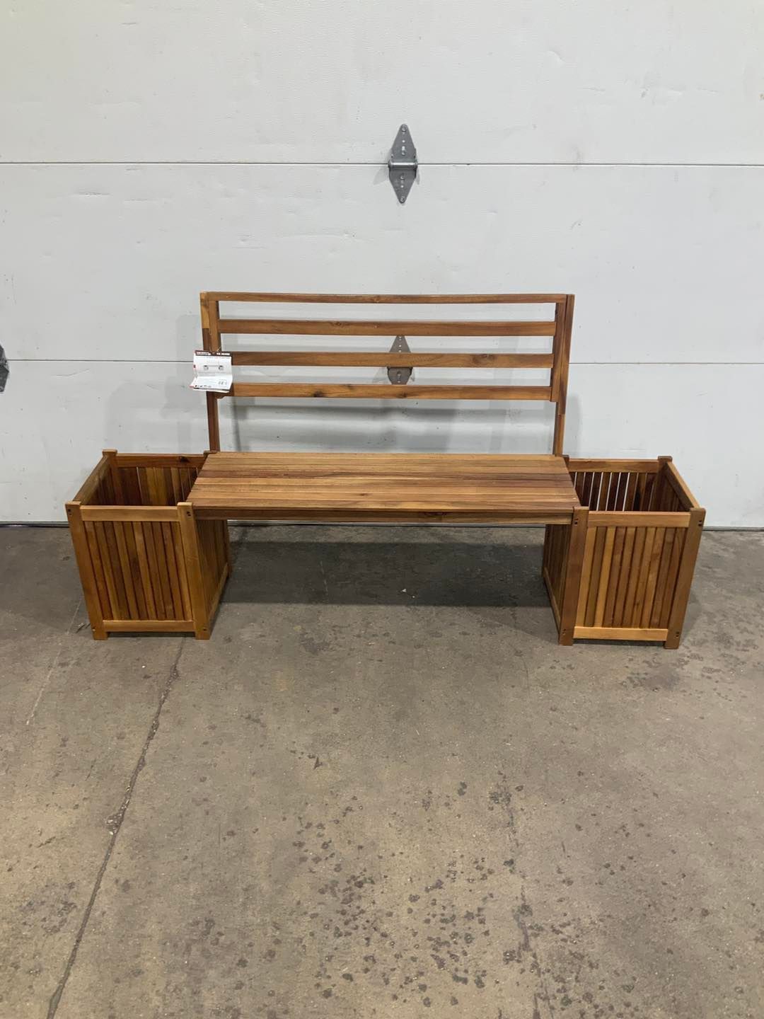 A wooden bench with two planters attached to it is sitting in front of a garage door.
