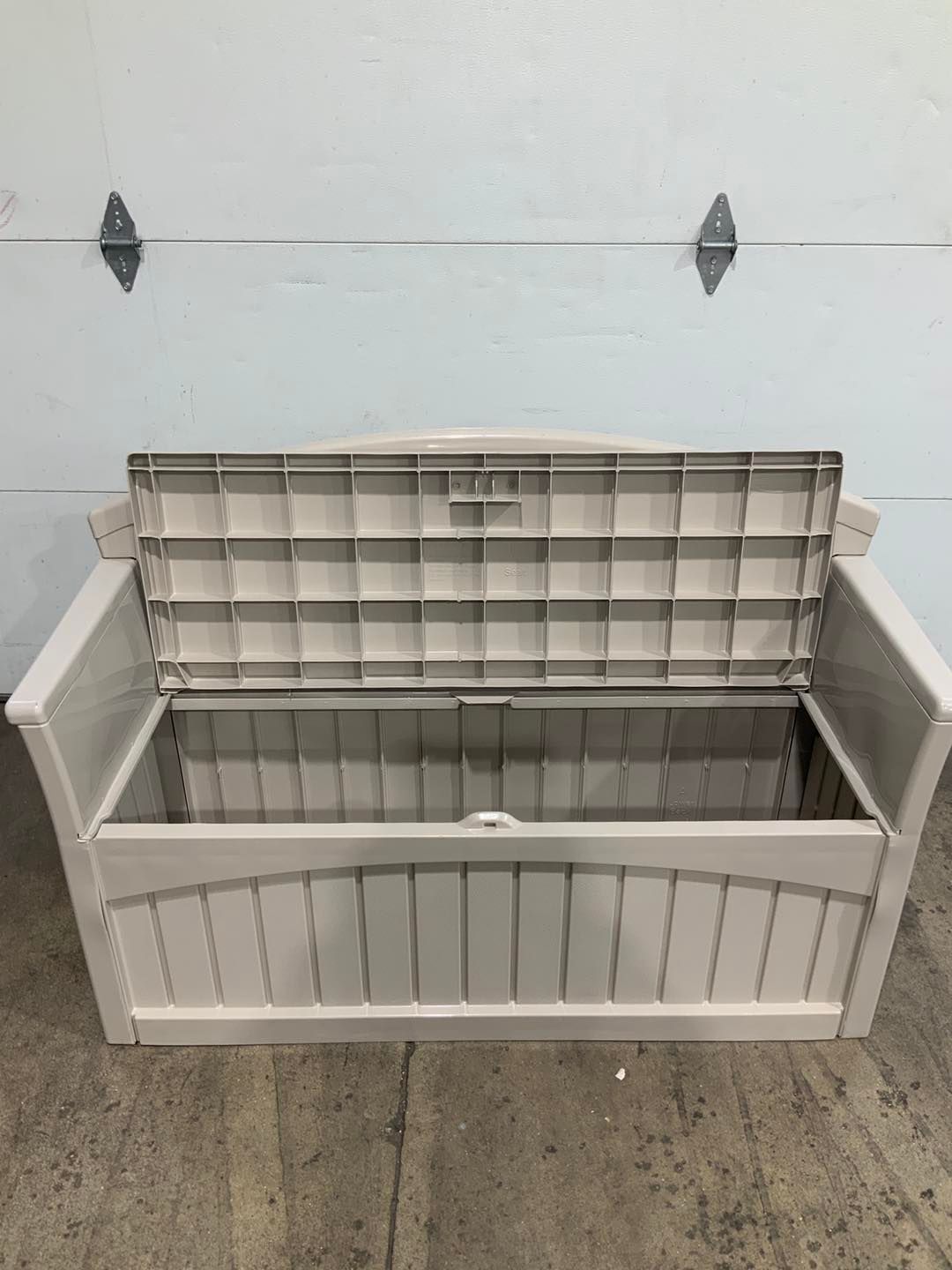 A white plastic bench with the lid open is sitting in front of a garage door.