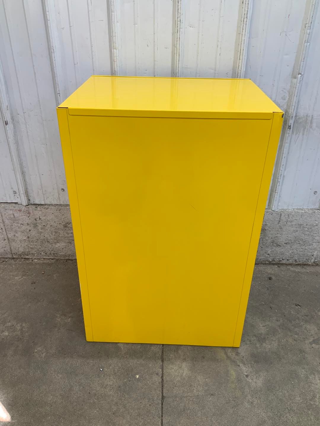 A yellow cabinet is sitting on the sidewalk in front of a white wall.