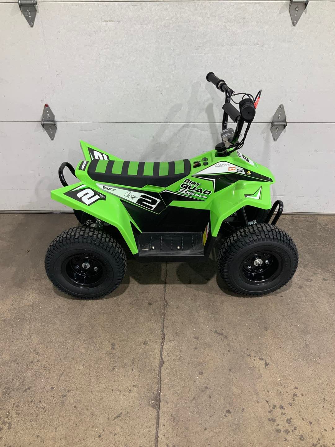 A green atv is parked in front of a garage door.