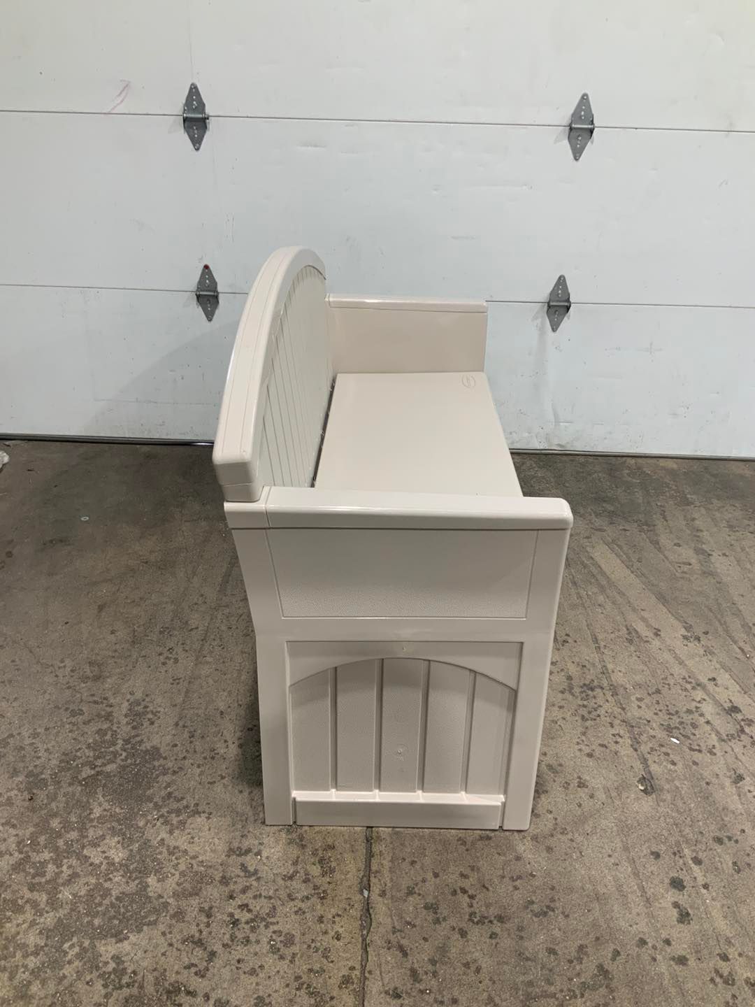 A white bench is sitting in front of a garage door.