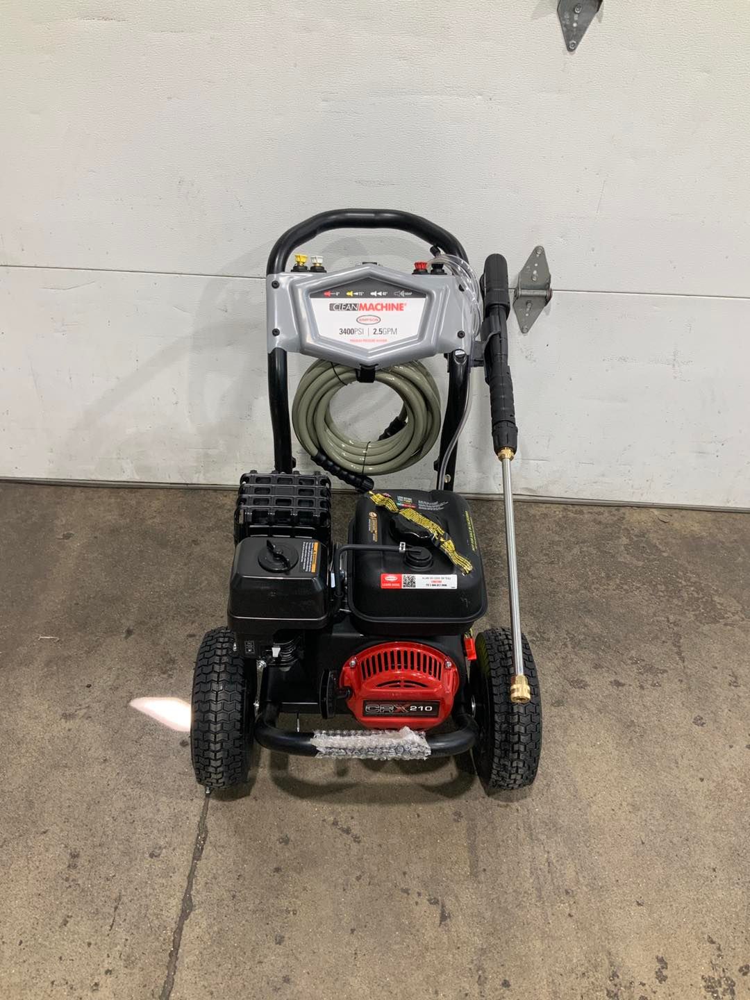 A gas powered pressure washer is sitting on the ground in front of a garage door.