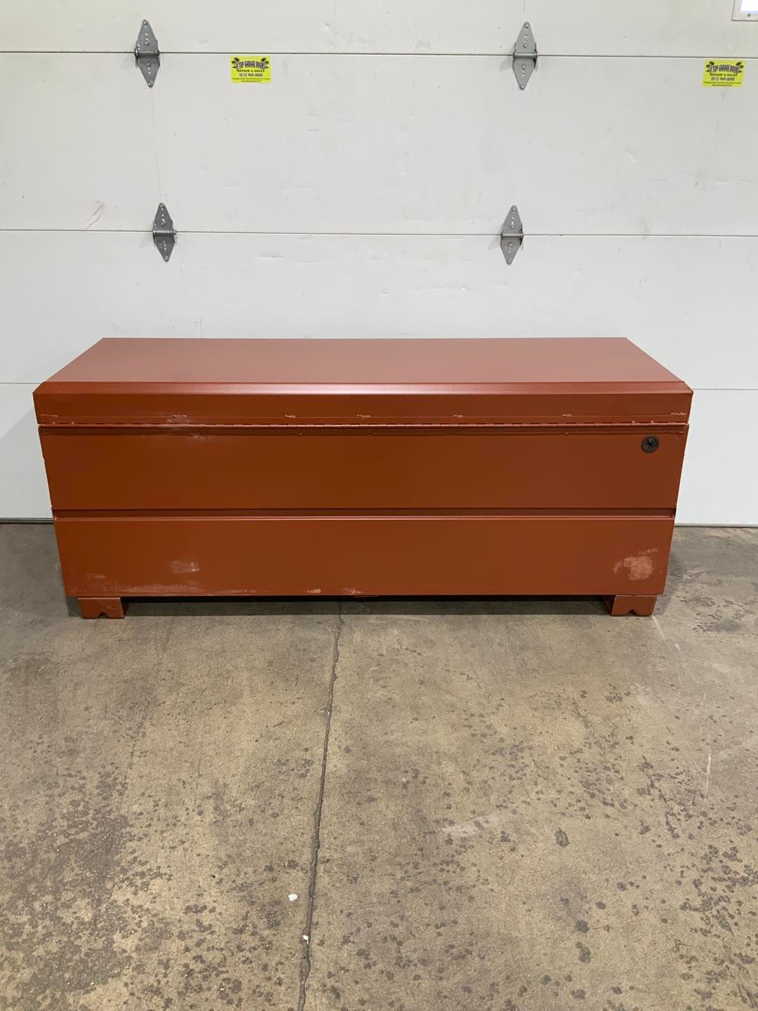 A red trunk is sitting in front of a garage door.