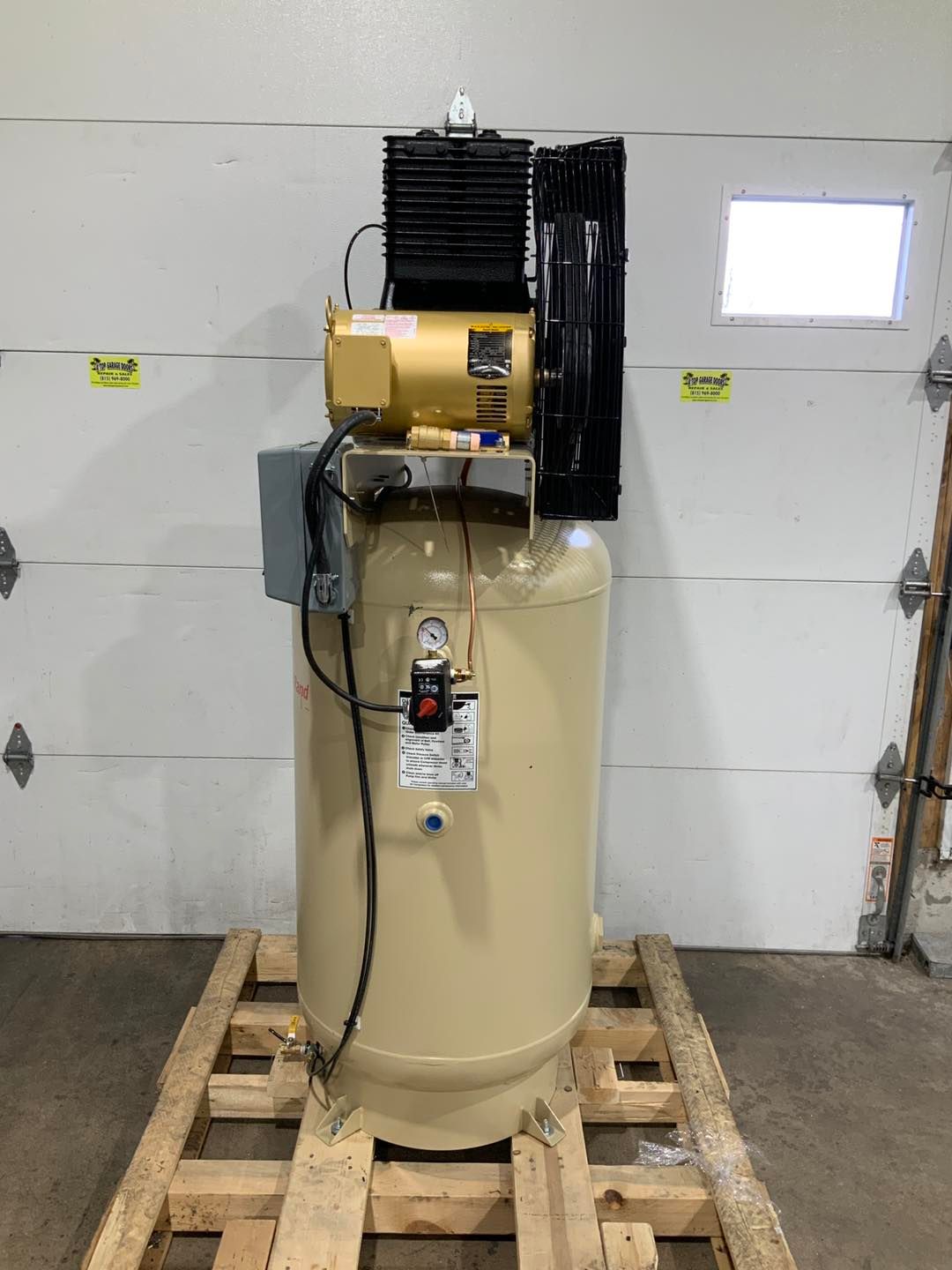 A large air compressor is sitting on a wooden pallet in front of a garage door.