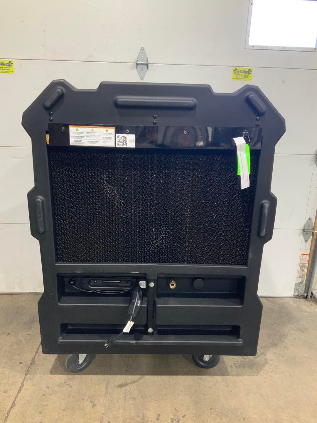 A black cooler with wheels is sitting in front of a garage door.