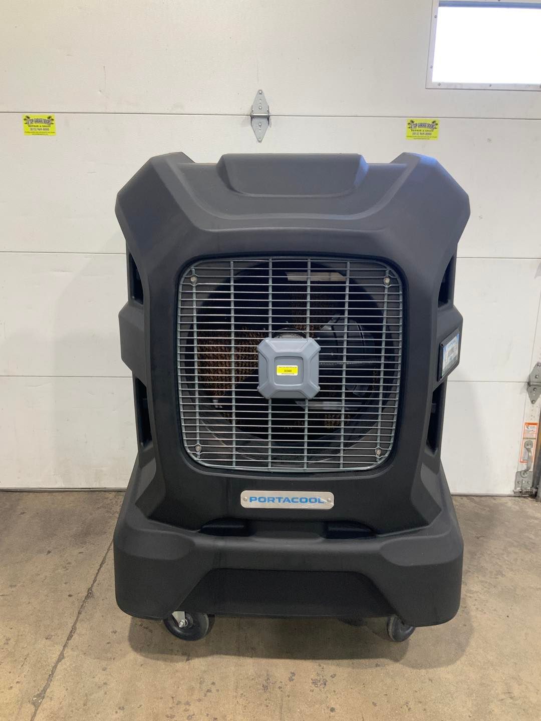 A large black fan with wheels is sitting in front of a garage door.