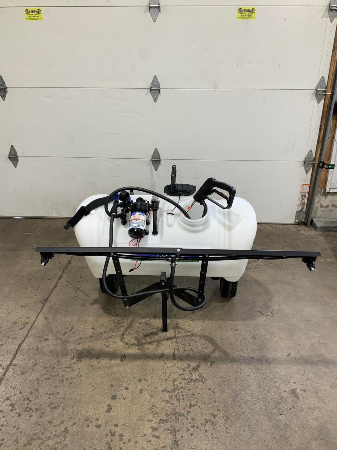 A white sprayer is sitting in front of a garage door.