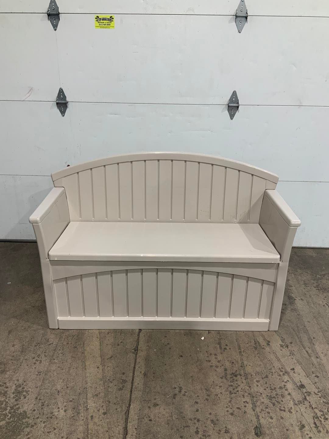 A white bench is sitting in front of a garage door.