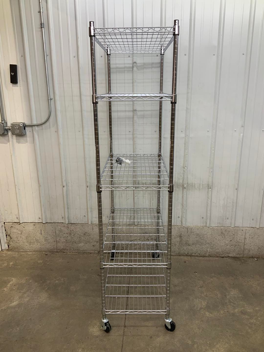 A metal shelf with wheels is sitting on the ground in front of a white wall.