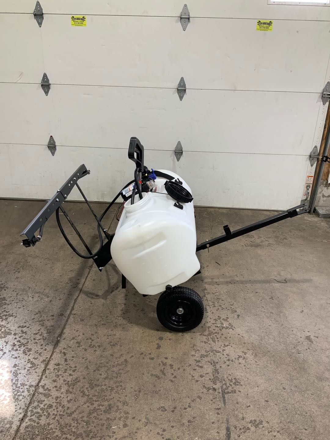 A sprayer is sitting on a cart in front of a garage door.