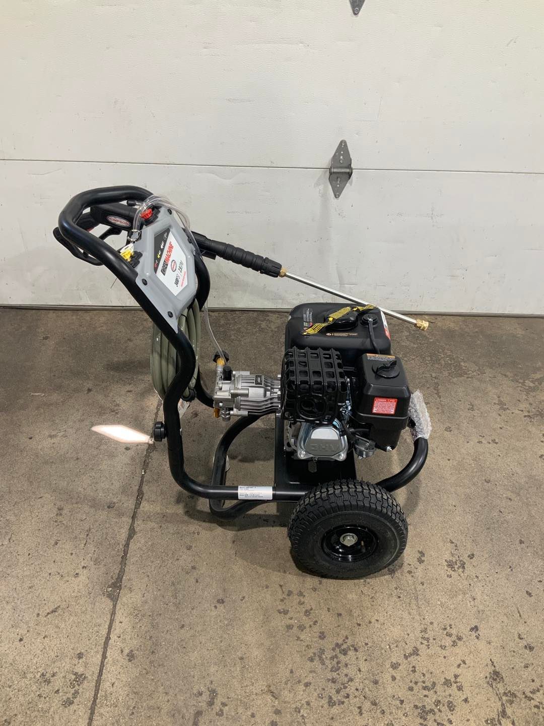 A gas powered pressure washer is sitting on the ground in front of a garage door.
