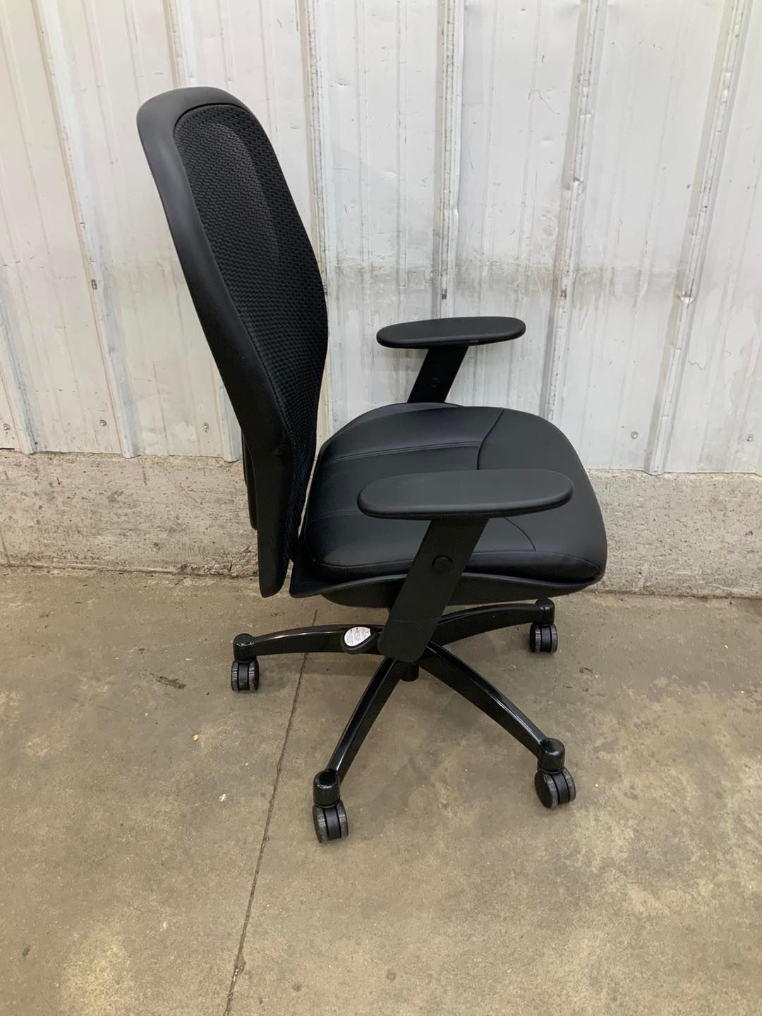 A black office chair is sitting on the ground in front of a white wall.