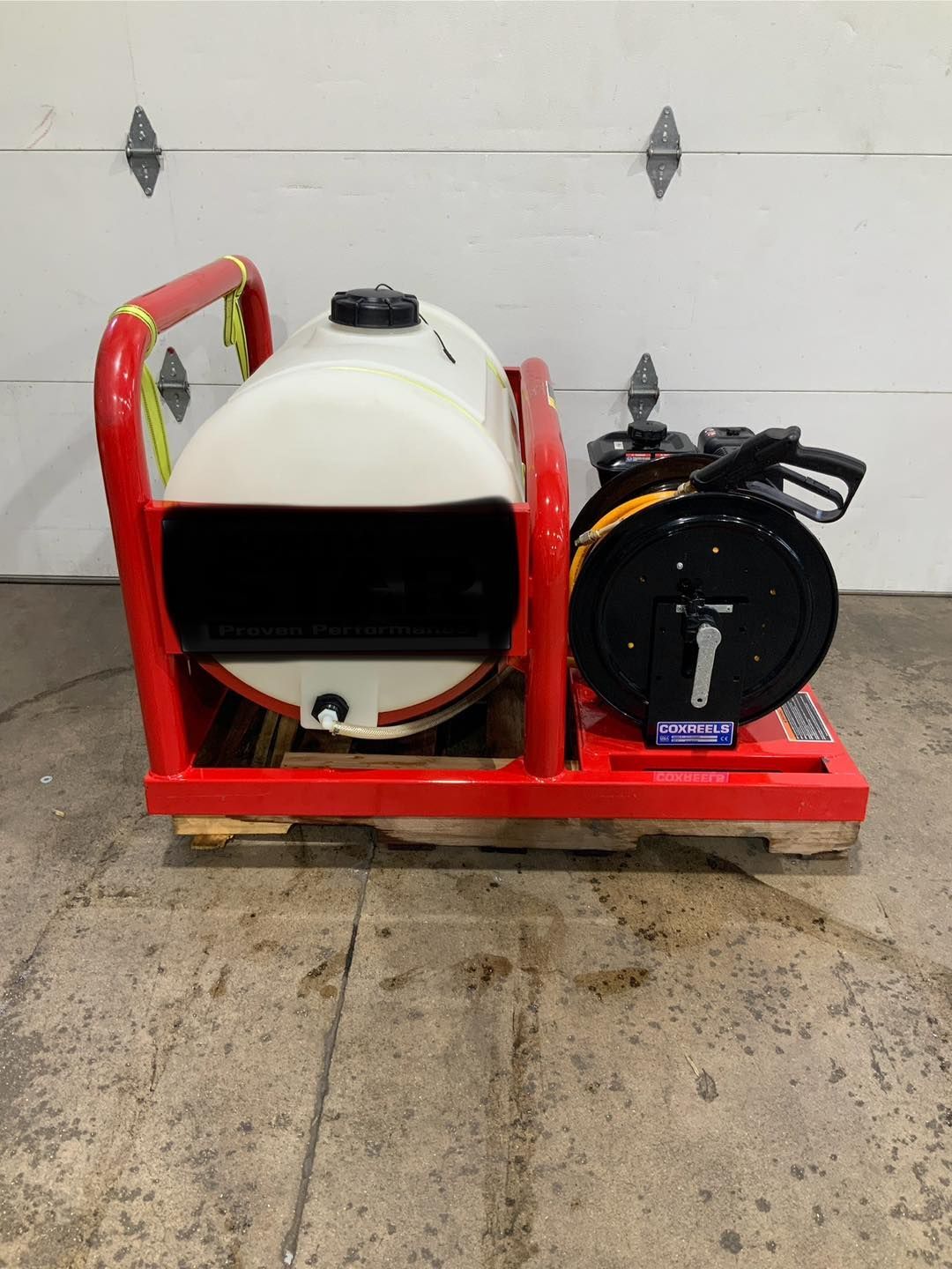 A red and white tank is sitting on a pallet in front of a garage door.