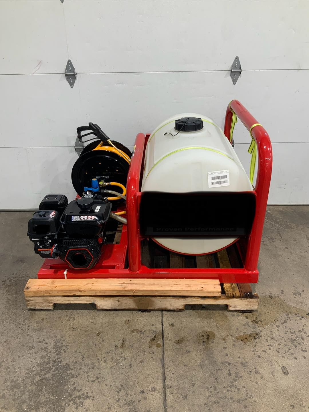 A red and white machine is sitting on a wooden pallet in front of a garage door.