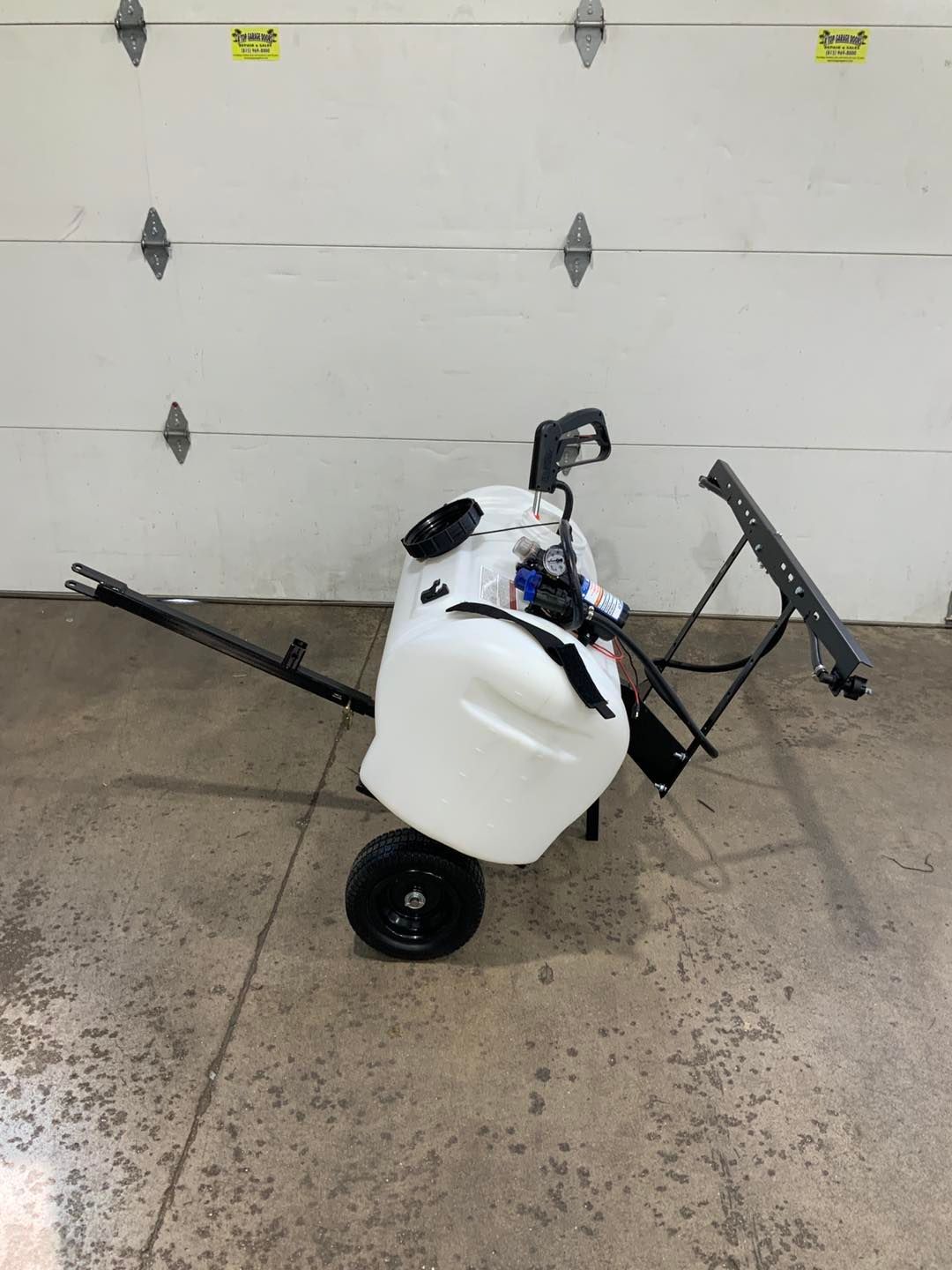 A sprayer is sitting on a cart in front of a garage door.